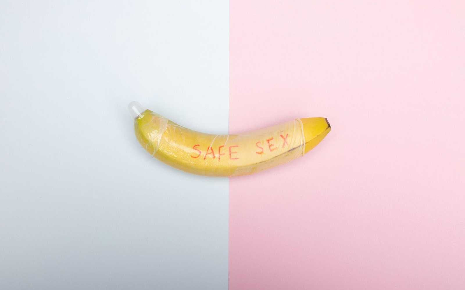 Image of a banana with Safe Sex written on it with a split grey and pink background.