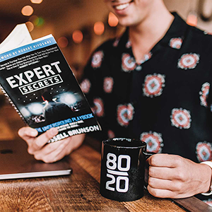Image of person holding Expert Secrets book for online marketing and an 80 20 mug